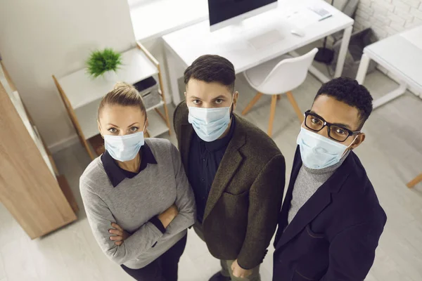 Group of company workers in face masks standing in office and looking at camera — Stock Photo, Image