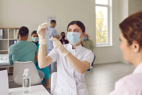 마스크를 쓴 젊은 간호사가 환자에게 주사를 하기 전에 유리병에서 백신을 꺼내는 모습 — 스톡 사진
