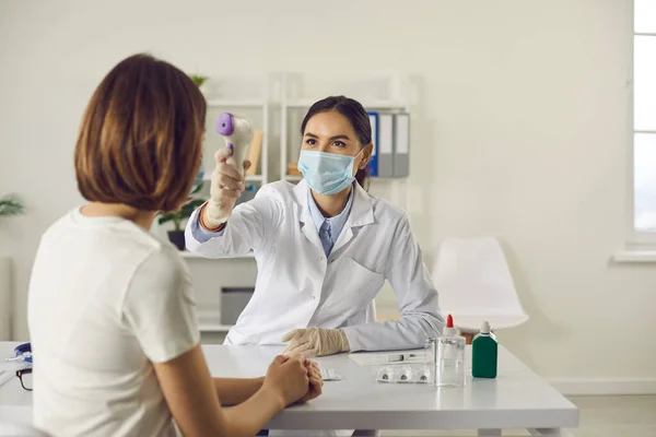 Sjuksköterska i ansiktsmask som mäter kvinnors kroppstemperatur med beröringsfri termometer — Stockfoto