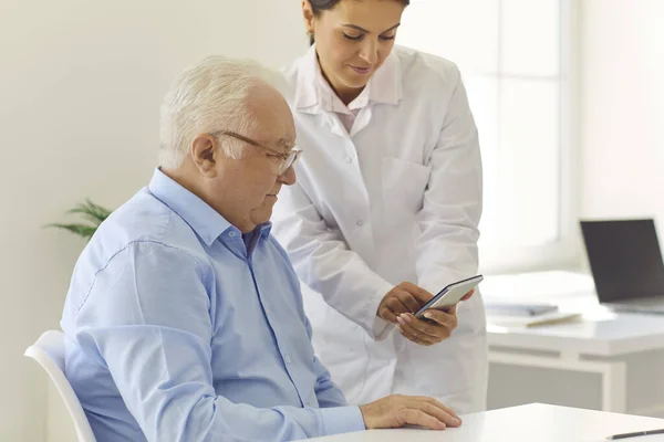 Pielęgniarka uczy staruszka korzystać z aplikacji telefonicznej do ustawiania przypomnienia o lekach lub śledzenia wskaźników zdrowia — Zdjęcie stockowe
