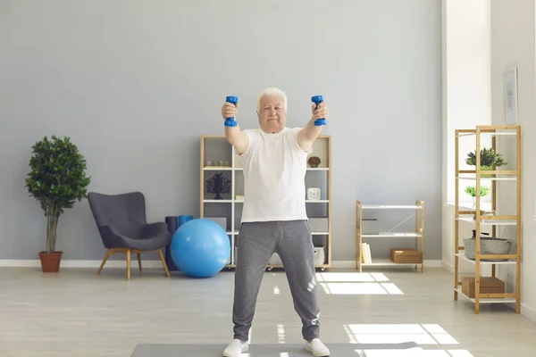 Determined senior man exercising with dumbbells during a routine sports workout at home