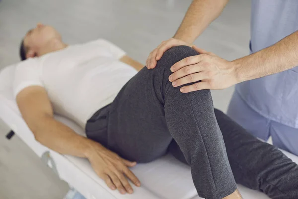 Hands of professional man chiropractor manual therapist fixing lying patients knee in stable position —  Fotos de Stock