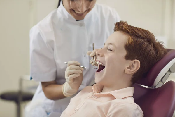 Female dentist examines the teeth of a little smiling boy with the help of special tools.