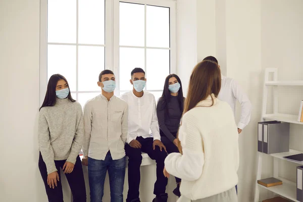 Группа офисных работников в медицинских защитных масках слушает презентацию женщины-коллеги — стоковое фото