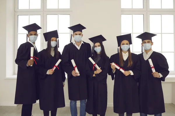 Group of diverse university or college graduates in face masks holding their diplomas — Stock Photo, Image