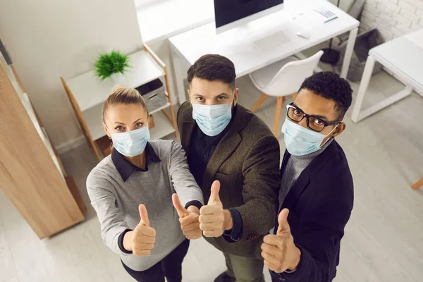 Young business people in medical face masks, looking at camera and giving thumbs-up — Stock Photo, Image