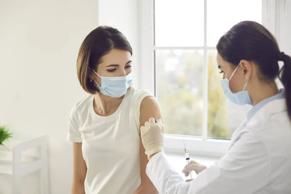 Young woman in a protective face mask getting an antiviral vaccine at the clinic — Foto de Stock