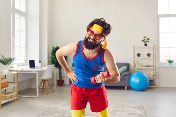 Смешной и выносливый мужчина в разноцветной спортивной одежде занимается спортом с гантелями дома. — стоковое фото