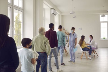 Doktor, aşı için gelen insanlardaki sıcaklığı temas olmayan kızılötesi termometreyle kontrol ediyor..