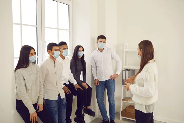 Jovens trabalhadores mascarados ouvindo gerente ou treinador em uma reunião durante a pandemia de Covid-19 — Fotografia de Stock