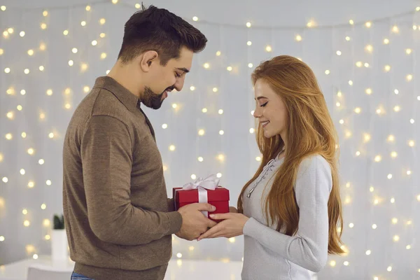 Νεαρό ευτυχισμένο χαμογελαστό ζευγάρι στέκεται και δίνει δώρα κατά τη διάρκεια των διακοπών στο σπίτι — Φωτογραφία Αρχείου