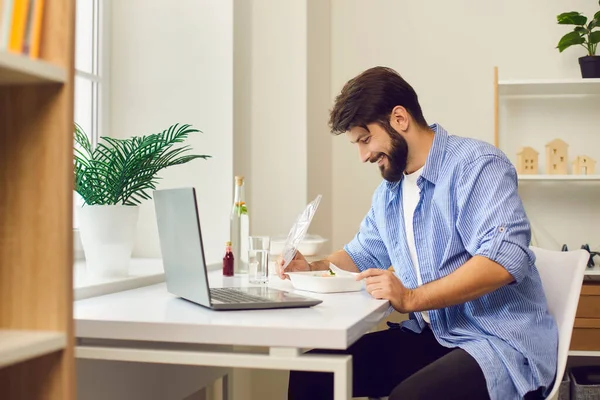 Glücklicher junger Mann genießt frische gesunde Mahlzeit zum Mitnehmen in der Mittagspause bei der Arbeit — Stockfoto