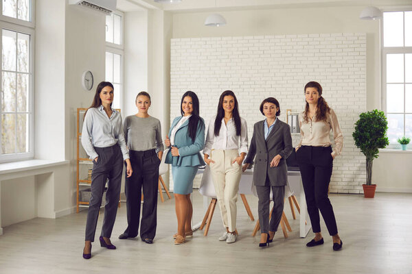 Группа уверенных молодых женщин, стоящих в офисе компании и смотрящих в камеру