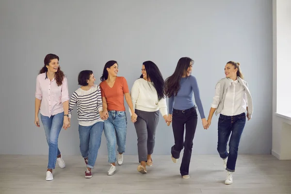 Groep vrolijke, zelfverzekerde vrouwen die hand in hand lopen en blijk geven van wederzijdse steun en solidariteit — Stockfoto