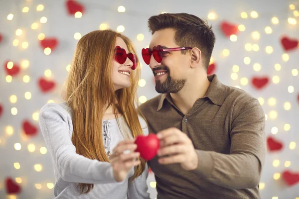 Mladí manželé se něžně podívají jeden do druhého a drží malé červené srdce. — Stock fotografie
