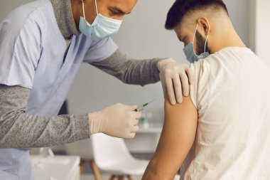 Yüz maskeli doktor aşı kampanyası sırasında hastaya antiviral aşı enjekte ediyor.