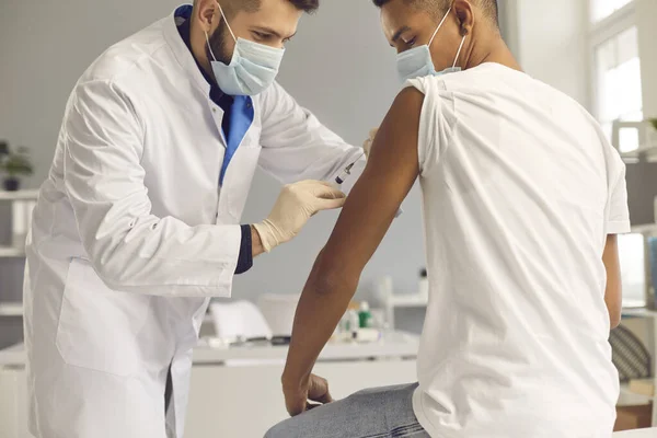 Ung läkare i ansiktsmask som ger coronavirus eller influensavaccin till patienten — Stockfoto