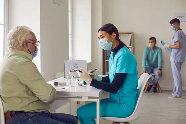 Aziatische vrouwelijke arts interviewt een oudere man die naar het ziekenhuis kwam voor vaccinatie. — Stockfoto