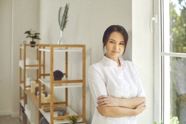Güzellik salonunda dikilip kameraya bakan ciddi bir profesyonel güzellik uzmanı.