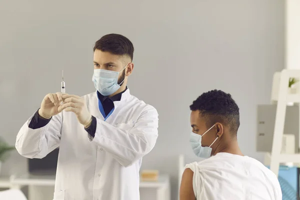 Ung läkare i ansiktsmask förbereder sprutan innan vaccinet ges till patienten — Stockfoto