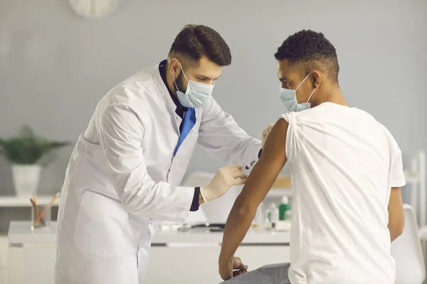 Arzt mit medizinischer Gesichtsmaske gibt jungen Patienten während Impfkampagne Impfstoff — Stockfoto