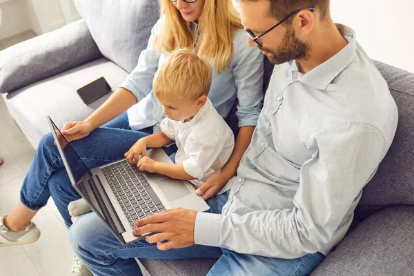 Семья с маленьким сыном сидит на диване и смотрит фильм на ноутбуке или общаться в Интернете — стоковое фото
