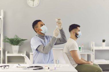 Genç Afro-Amerikalı doktor, hastaya enjekte etmeden önce şişeden aşı çıkarıyor.