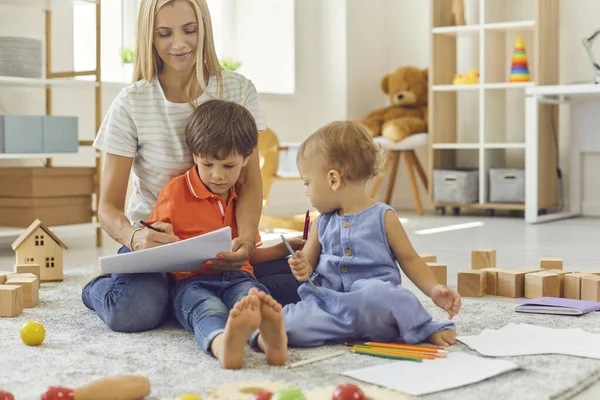 Щаслива мати з двома маленькими синами сидить на підлозі і малює на папері . — стокове фото
