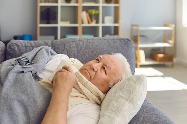 Droevige senior man in sjaal liggend in bed met zakdoek onder deken en zich ziek voelen — Stockfoto