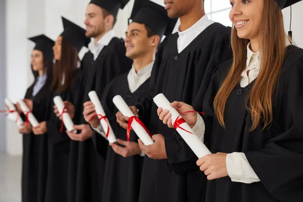 Skupina multietnických lidí stojí v řadě a v rukou drží svitky diplomů. — Stock fotografie