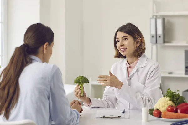 Näringsfysiker som håller i broccoli och berättar för unga kvinnor om fördelarna med hälsosam kost — Stockfoto