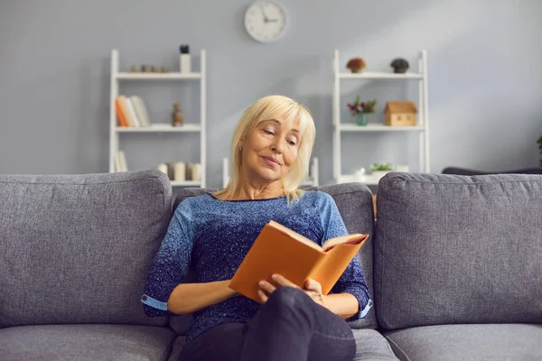 Donna di mezza età in abbigliamento casual seduta sul divano e libro di lettura — Foto Stock