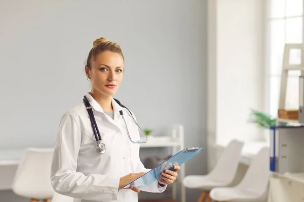 Portrait d'une jeune femme médecin confiante debout avec un presse-papiers dans ses mains. — Photo