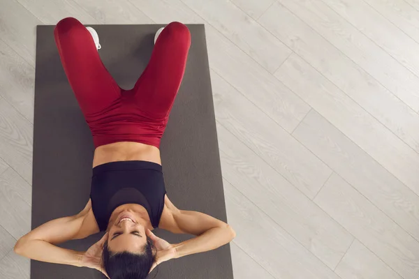 Lachende jonge fitness slanke vrouw in sportkleding zitten op fitmess mat en kijken naar de camera — Stockfoto