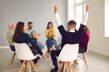 Diverse group therapy members applauding happy young man who overcame his addiction clipart