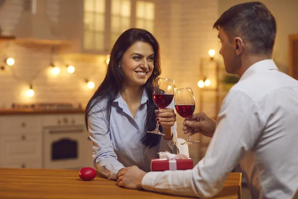 Jovem casal amoroso sentado na cozinha, de mãos dadas, bebendo vinho durante o dia dos namorados — Fotografia de Stock