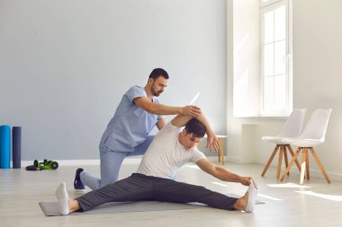 Fizyoterapist, genç bir adamın rehabilitasyon sırasında esneme egzersizi yapmasına yardım ediyor.