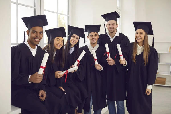 Skupina spokojených absolventů mezinárodních univerzit, kteří drží diplomy a dívají se do kamery — Stock fotografie