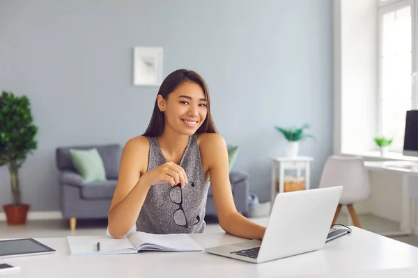 Lächelnde asiatische Büroangestellte, die in modernen, geräumigen Büros mit Laptop arbeitet — Stockfoto