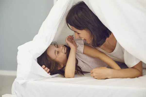 어머니와 취학 전의 딸은 집에서 담요 아래 침대에서 함께 재미있게 놀고 있다. — 스톡 사진