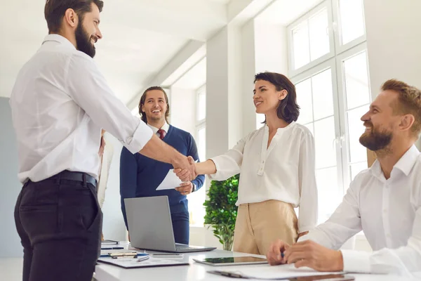 Un team di giovani imprenditori fiducioso incontra il suo cliente e stringe la mano in un ufficio luminoso e moderno. — Foto Stock