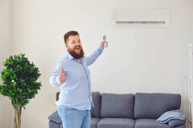 Komik sakallı adam klimayı uzaktan kumandayla açıyor ve dairede baş parmağını gösteriyor, boşluğu kopyalıyor.