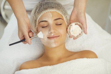 Dermatolog cilt bakımı sırasında kadınların yüzüne nemlendirici maske takıyor.