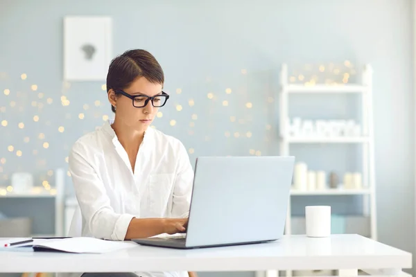 Junge Geschäftsfrau mit Brille stichelt und arbeitet von zu Hause aus am Laptop — Stockfoto