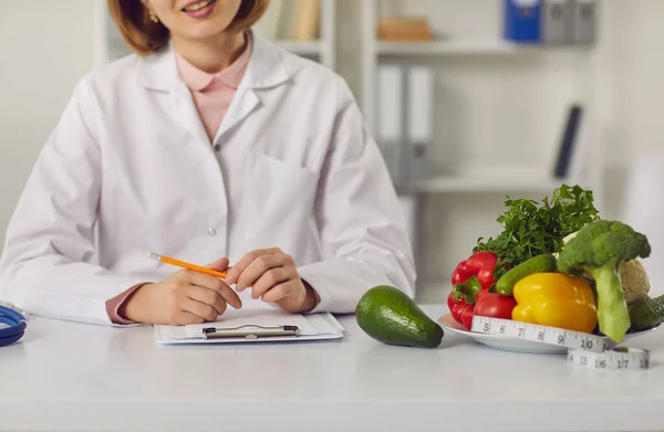 Dietista sentado a la mesa con frutas frescas, verduras y dieta individual —  Fotos de Stock