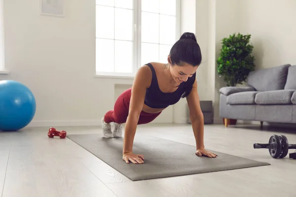 Vrolijke jonge vrouw doet volledige plank op sportmat tijdens fitness training thuis — Stockfoto