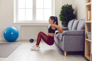Gülümseyen genç bayan sporcu evde kalça ve kol kasları için antrenman yapıyor.