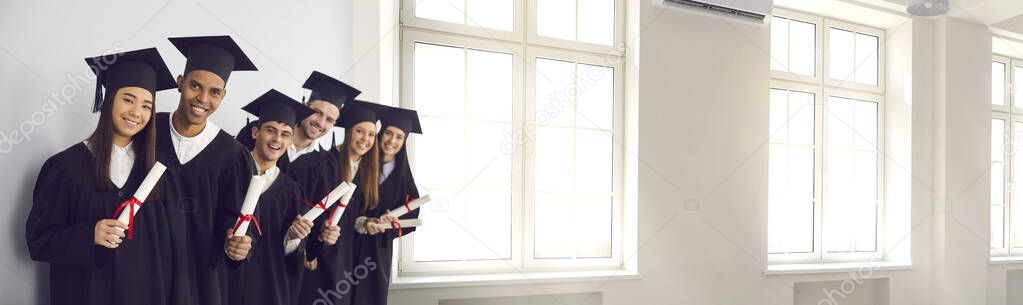 Banner with happy graduates holding diplomas and smiling in university hall with big windows