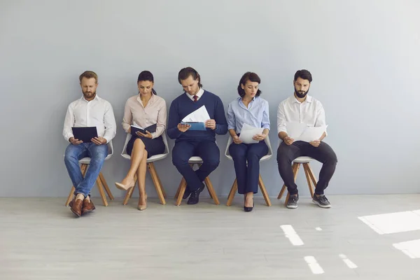 Grupp arbetssökande som sitter på stolar i rad med meritförteckningar och väntar i kö för intervju — Stockfoto
