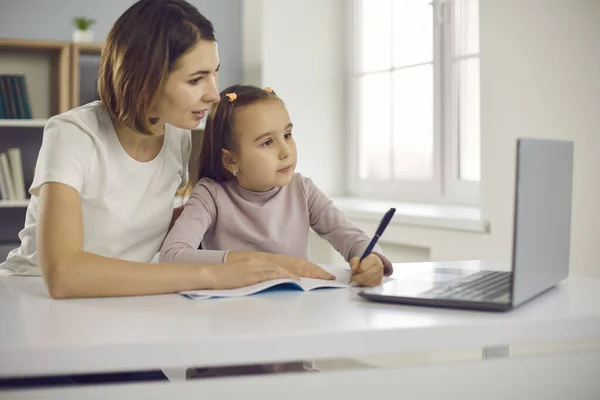 Маленькая позитивная девочка и ее мать рисуют или изучают алфавит и пишут во время онлайн урока — стоковое фото